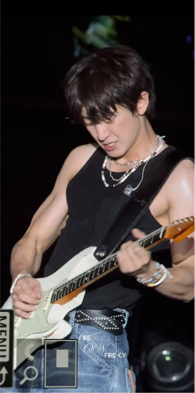 A guitarist in a black vest under stage lights