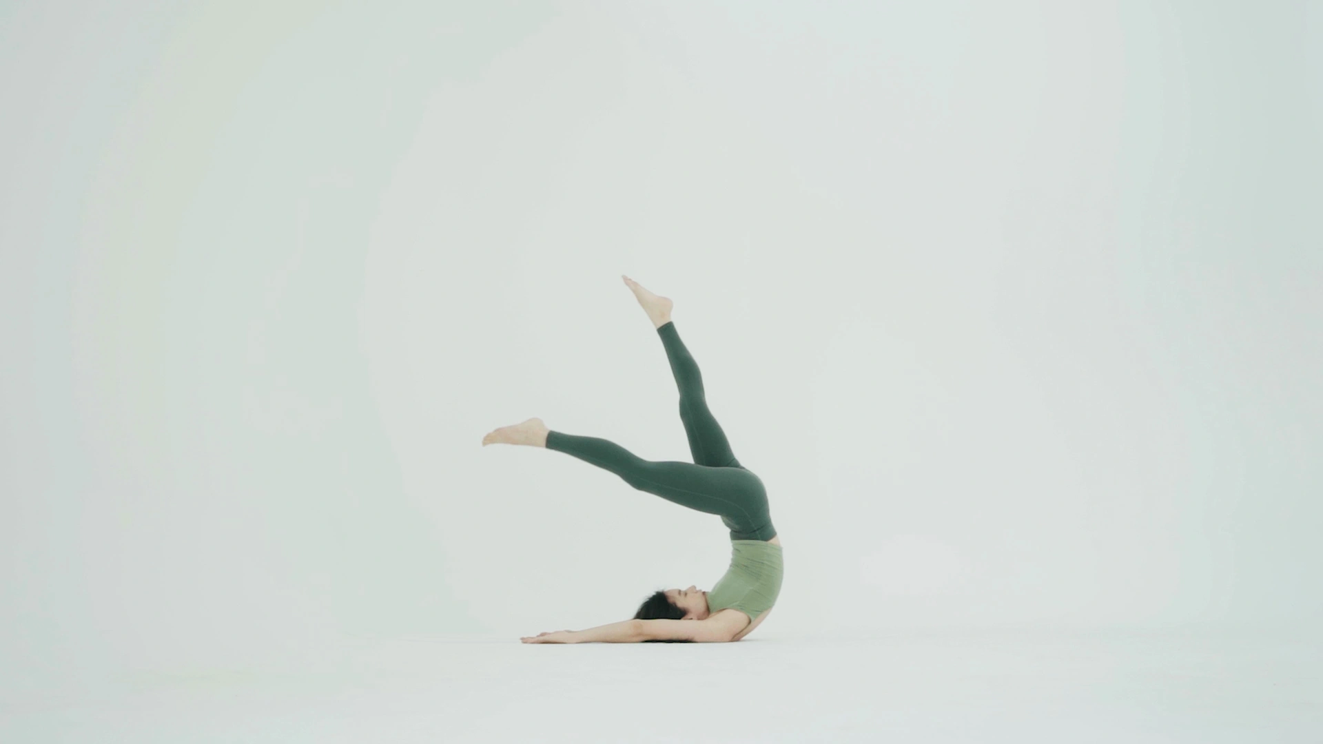 A balancing figure in green against a pale studio