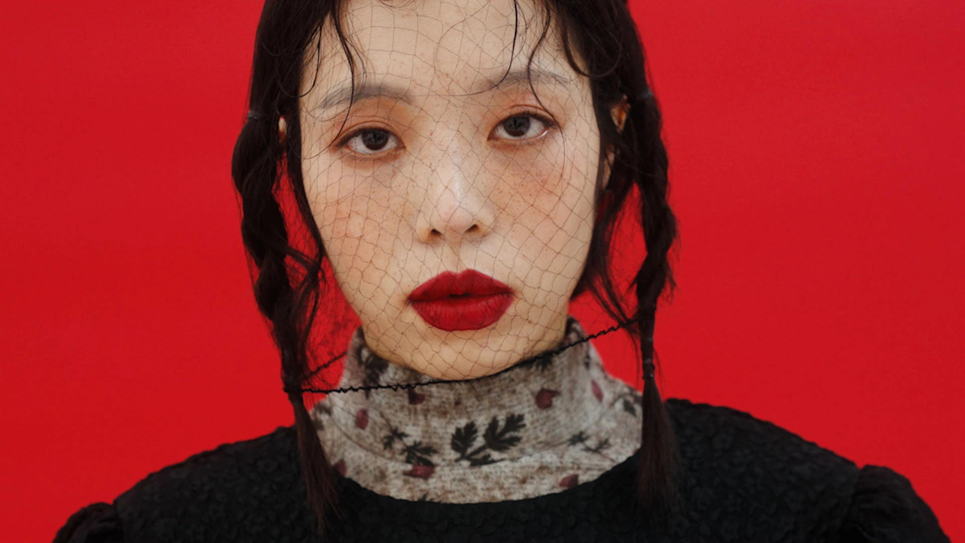 A red-lipped portrait on a vermilion background